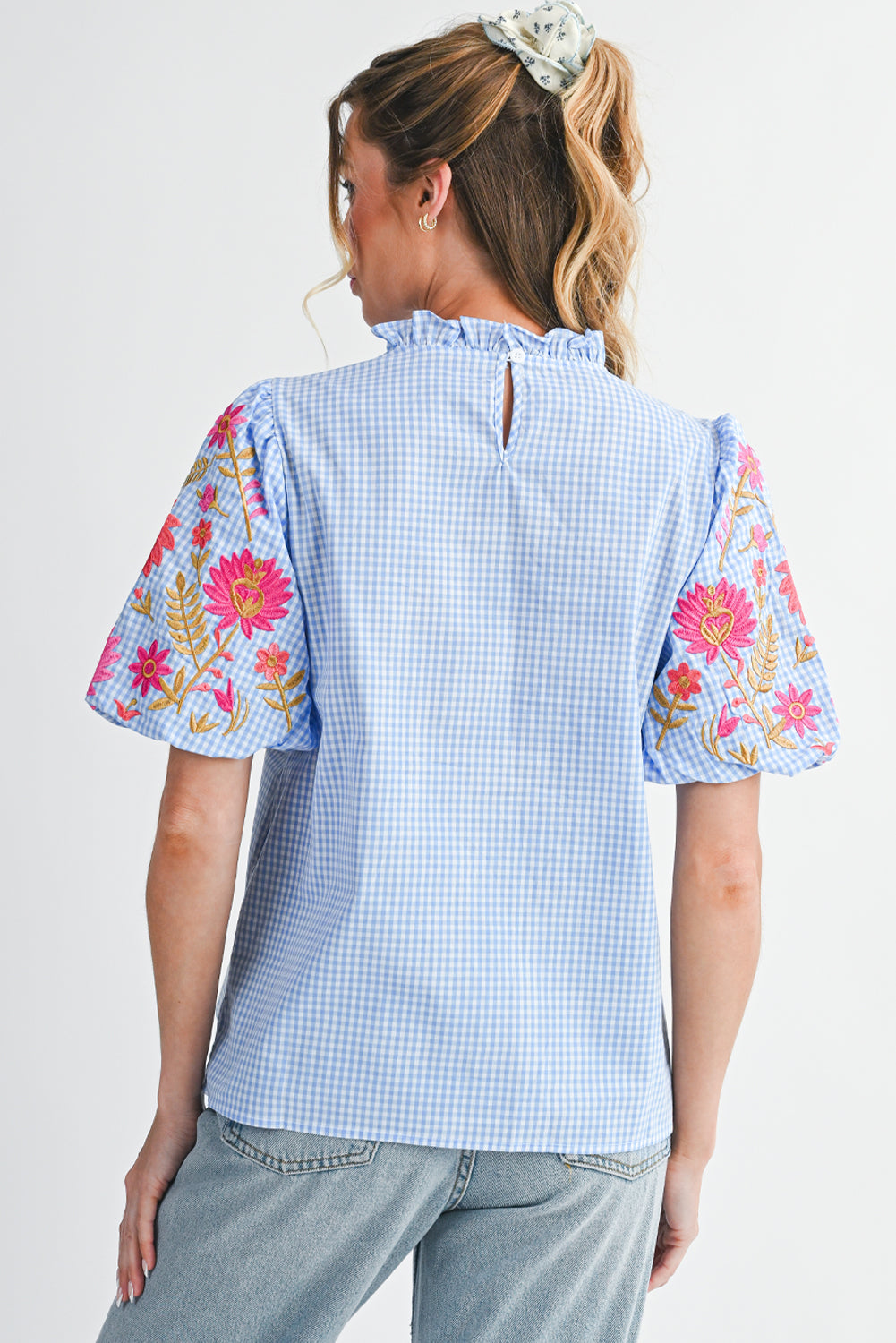 Woman wearing a light blue checkered top with floral sleeves on a white background