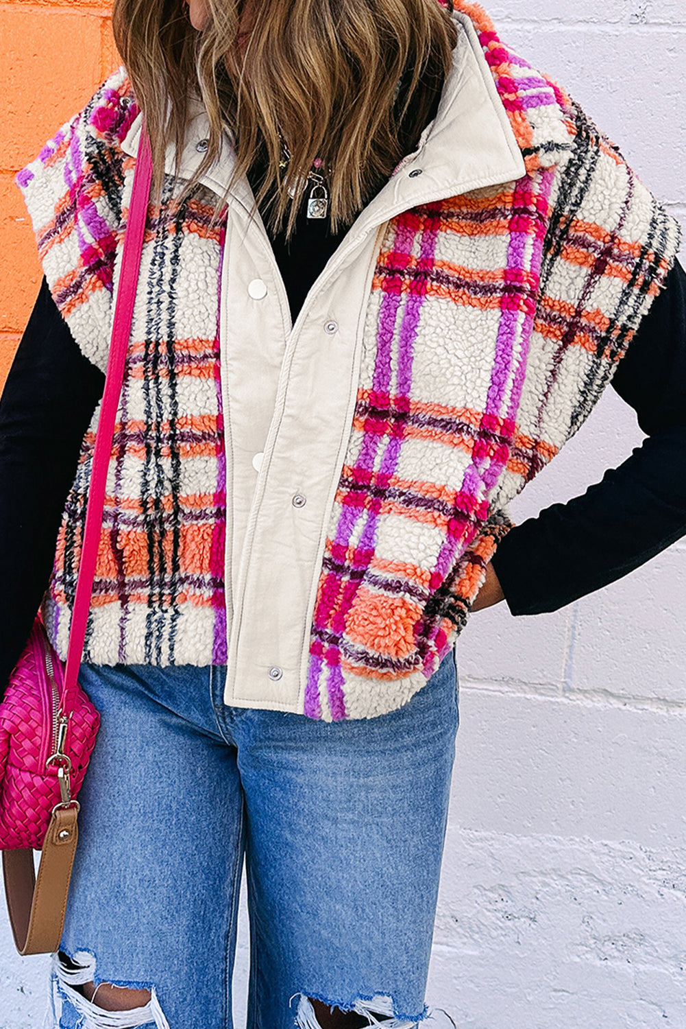 Person wearing a colorful plaid vest over a white shirt, blue jeans, and sneakers, with a pink bag.