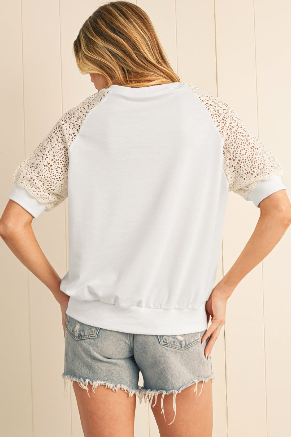 Person wearing a white lace-trimmed top and denim shorts against a light wooden panel background