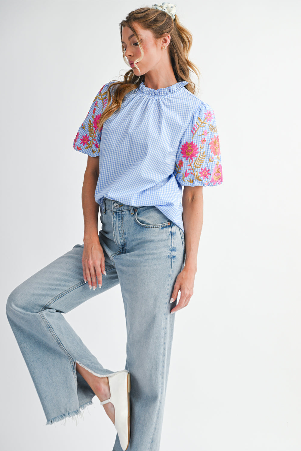 Woman wearing a light blue top with floral embroidery and jeans on a white background