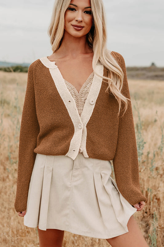 Woman wearing a brown cardigan over a white top and beige skirt in a field.