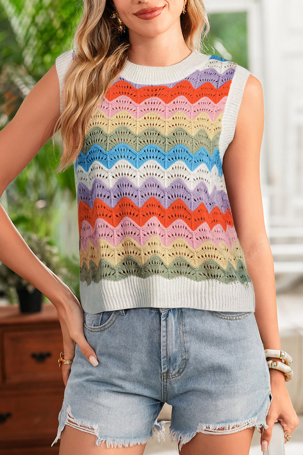 Person wearing a colorful sleeveless sweater and denim shorts indoors.