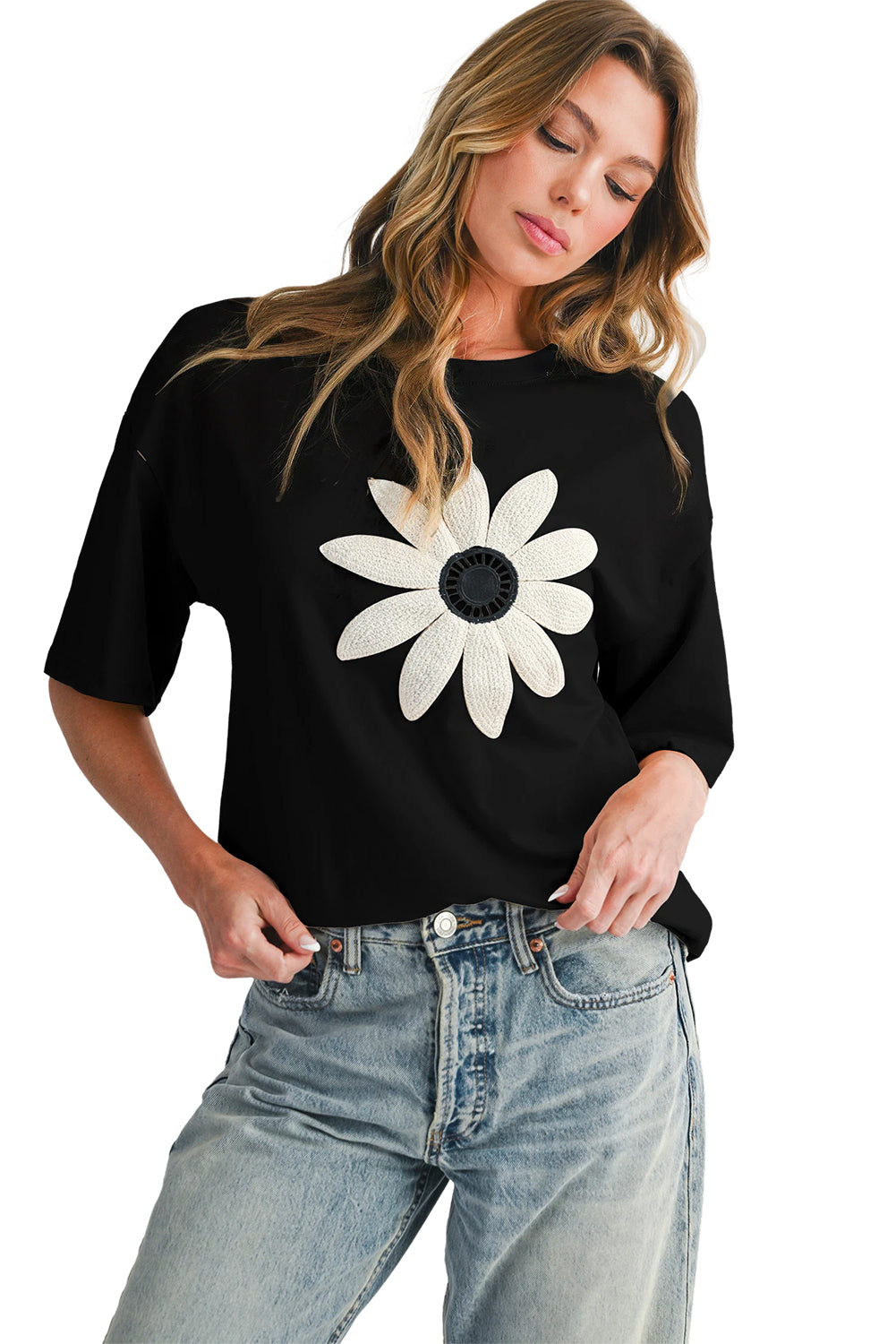 Woman wearing a black t-shirt with a white flower design and blue jeans on a white background
