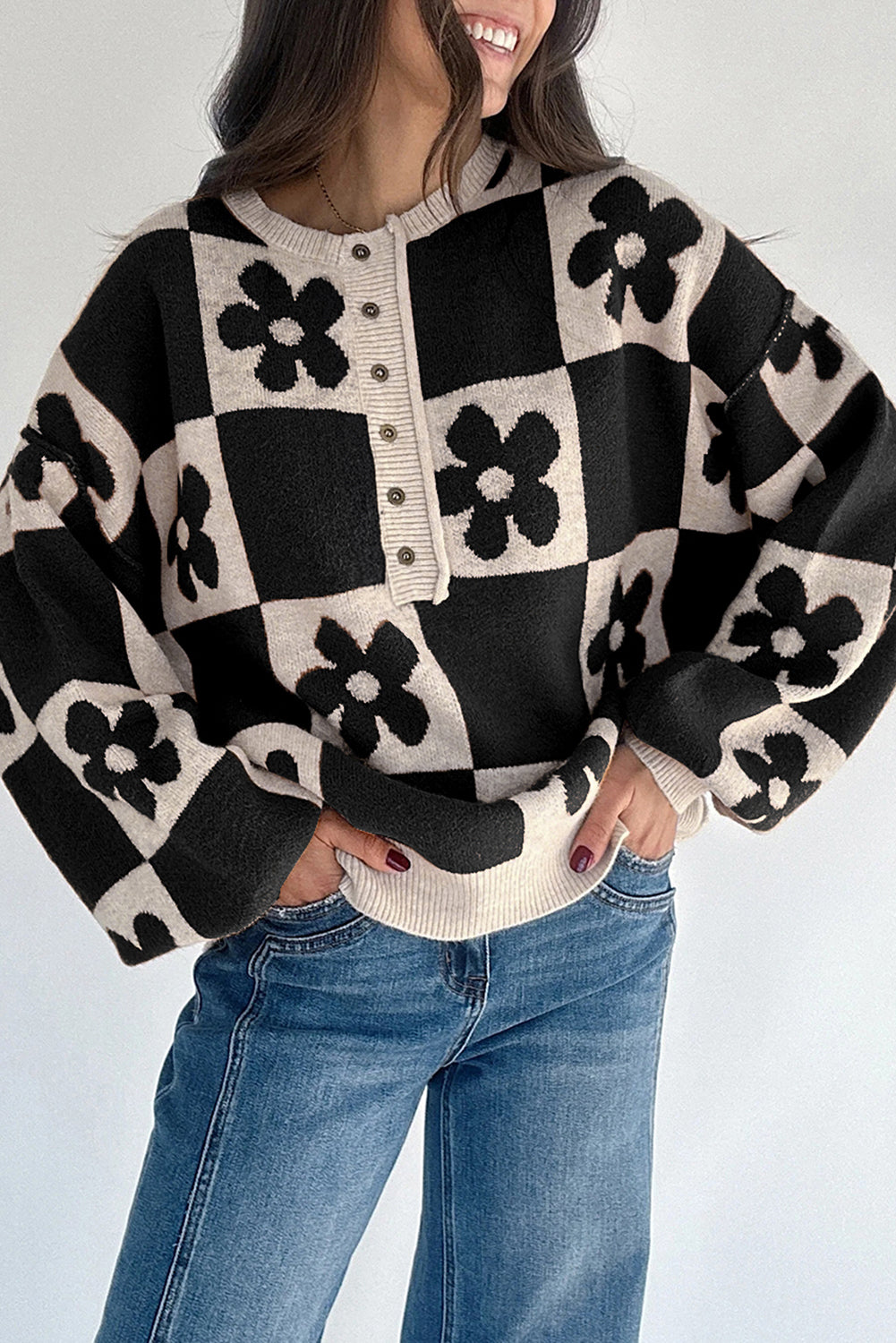 Person wearing a black and white checkered sweater with floral patterns and blue jeans on a light gray background