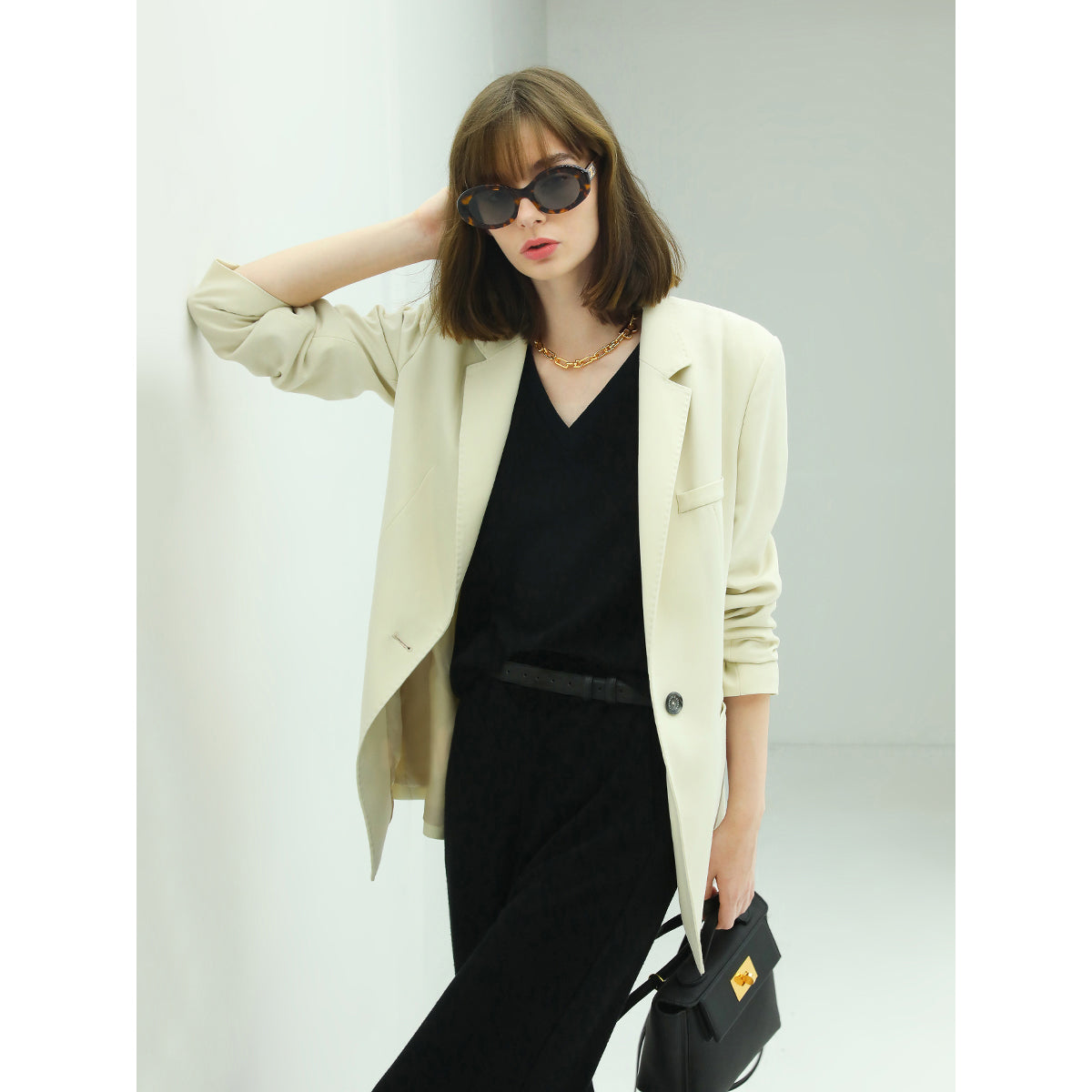 Woman wearing a beige blazer over a black outfit with sunglasses against a light background