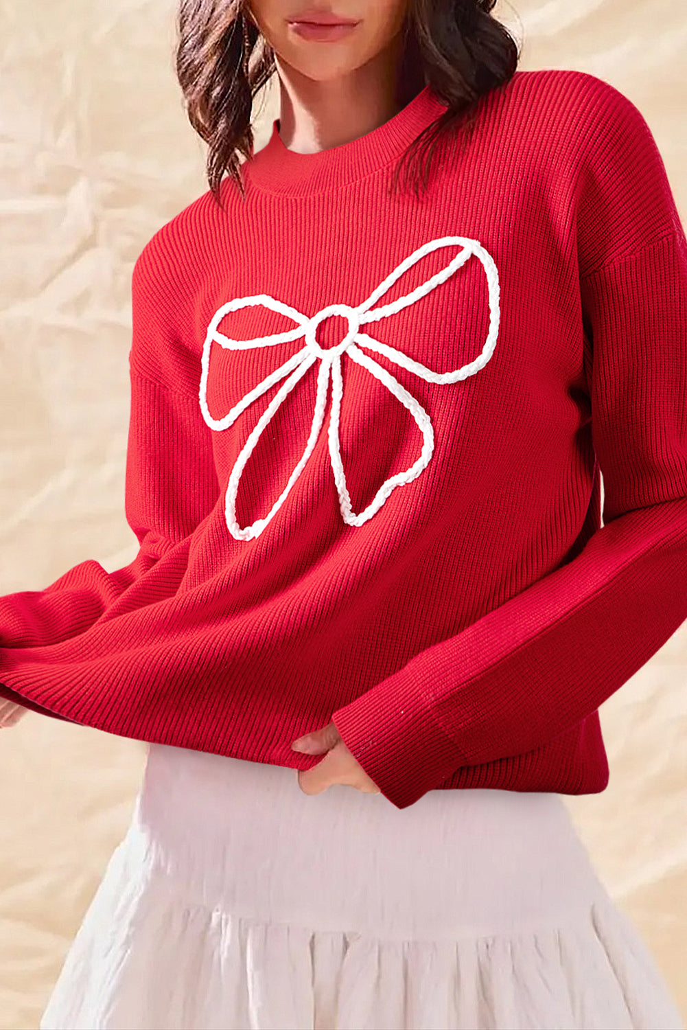 Red sweater with a white bow design worn by a person against a beige background