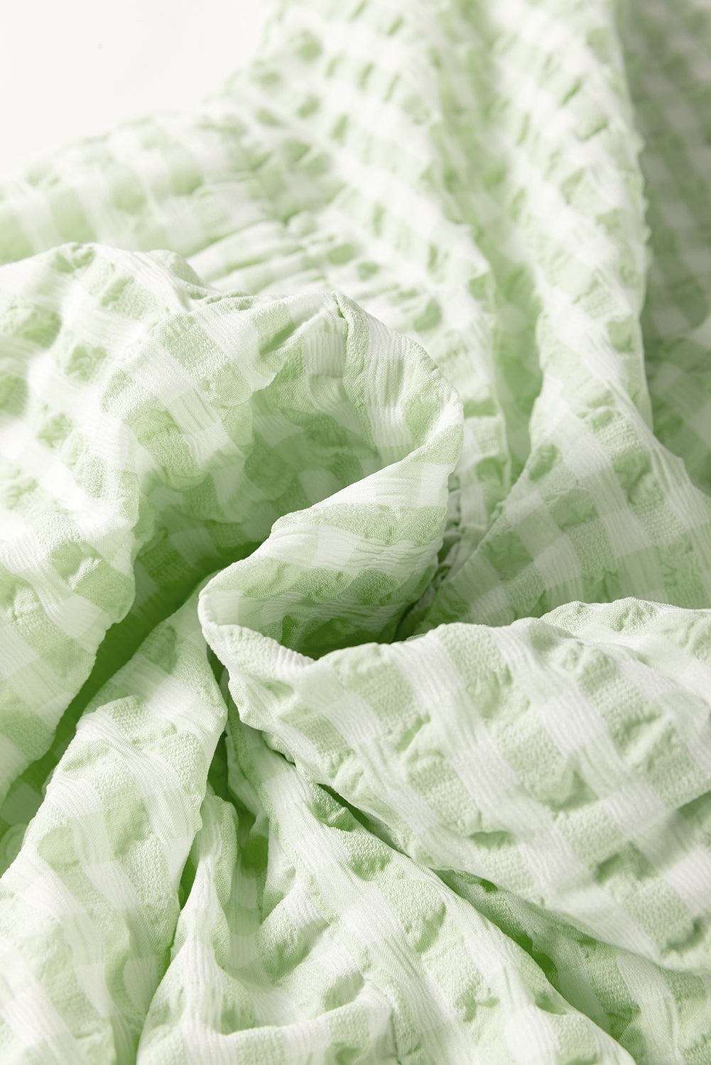 Fabric view of a light green plaid ruffle mini dress with short sleeves.