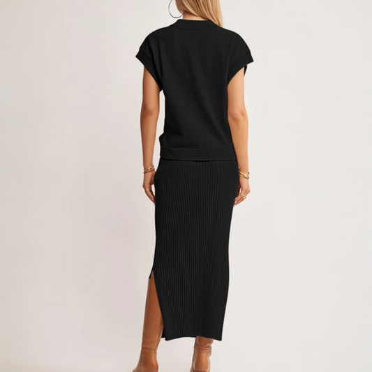 A rear view of a model in a black ribbed knit two-piece set, highlighting the midi-length skirt's side slit and the relaxed drape of the dolman tee.
