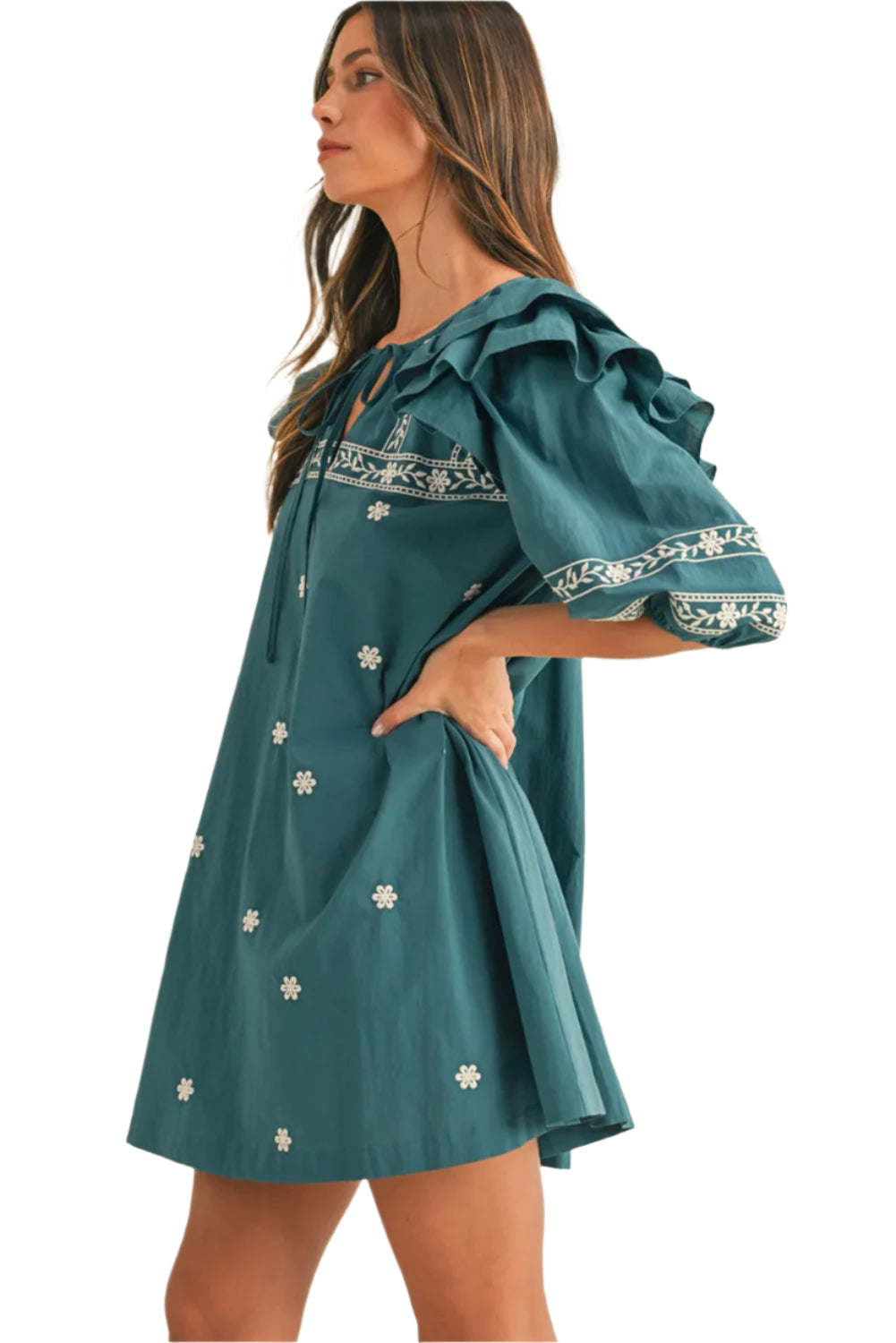 Side view of a woman wearing a teal boho mini dress with floral embroidery, puffed ruffle sleeves, and a tie-neck detail, showcasing a casual yet elegant style.