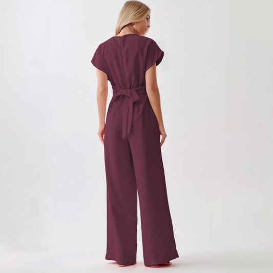 Rear view of a plum wide-leg jumpsuit showing the elegant tie-back knot at the waist and a streamlined, floor-length silhouette.