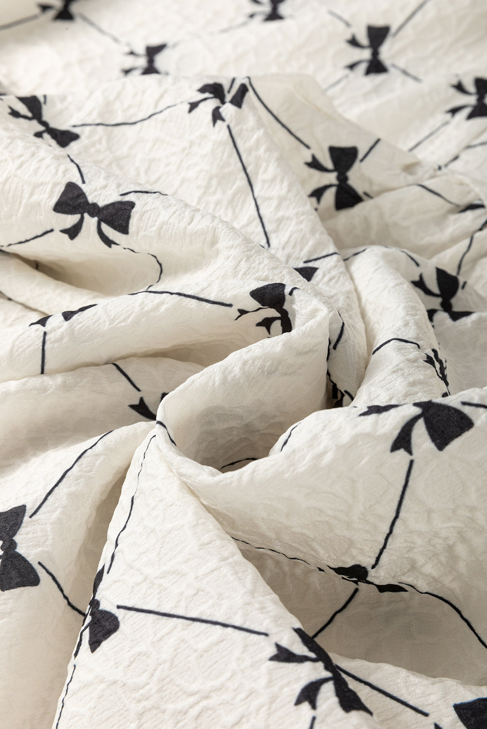 A white bow print with short lantern sleeves on a hanger. Fabric view.