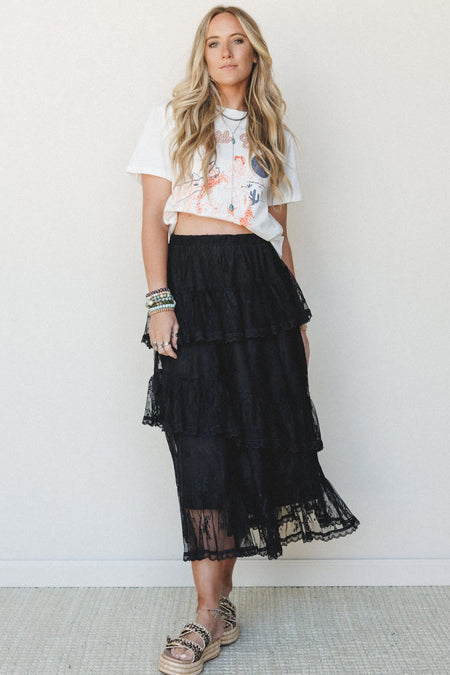 Woman's wearing a graphic tea and a black ruffled lace midi skirt.