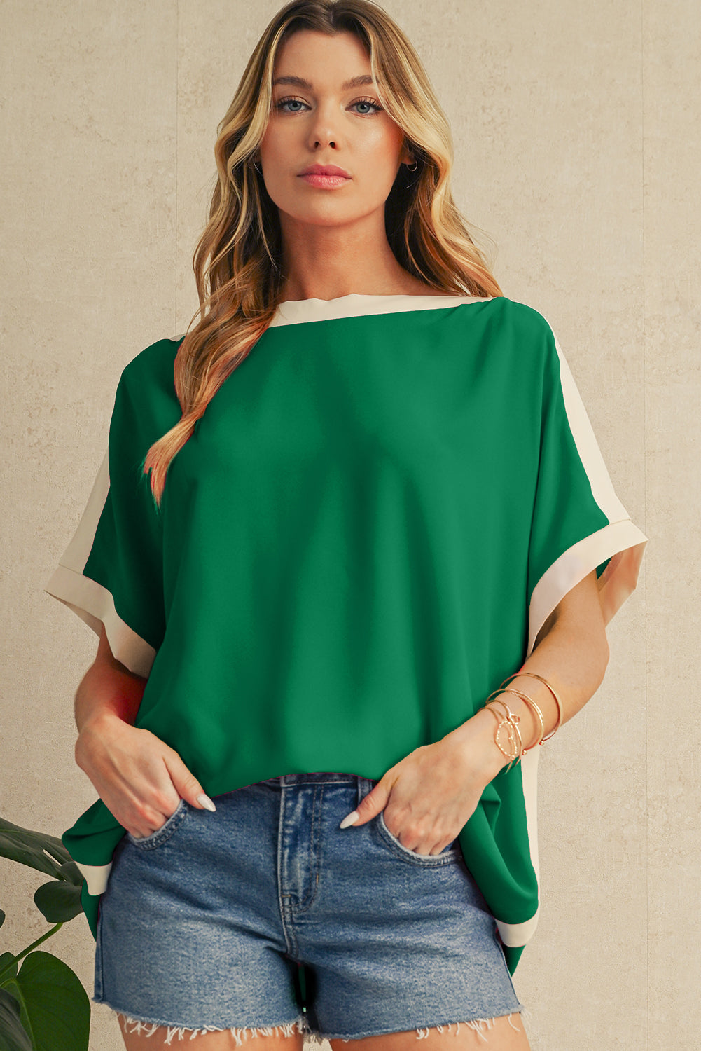Woman wearing a green top with white trim and denim shorts against a beige background