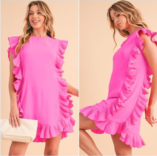 Bright pink ruffled dress with cascading pleats along the sides and hem, modeled by a smiling woman holding a white clutch in a soft beige background.