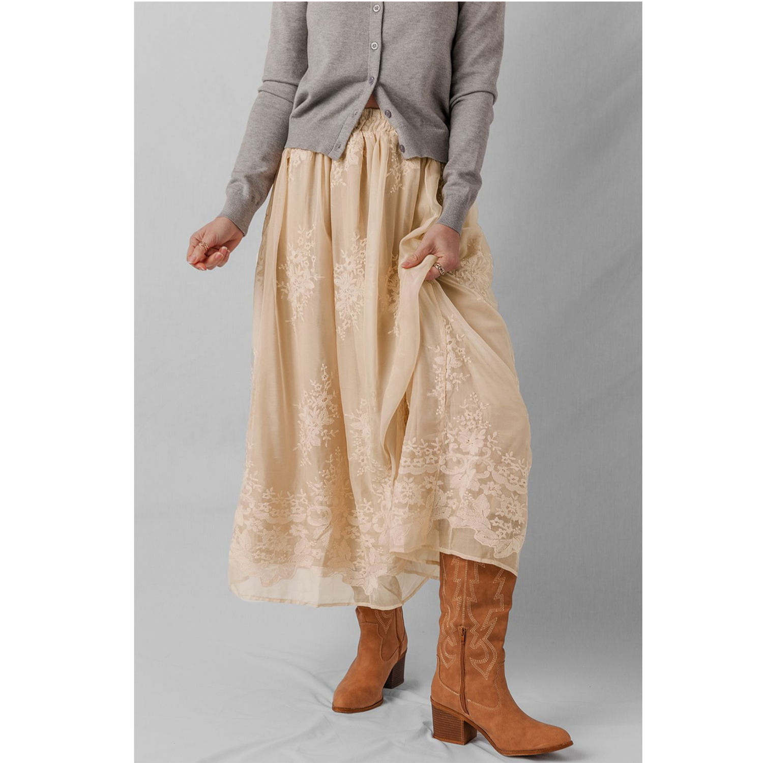 Person wearing a beige lace skirt and brown boots on a gray background