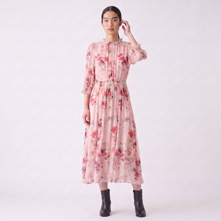 Asian model wearing a pink floral silk midi dress with three-quarter smocked sleeves, high ruffled neckline, and black leather ankle boots from the Catherine Martin Women's Dresses collection.