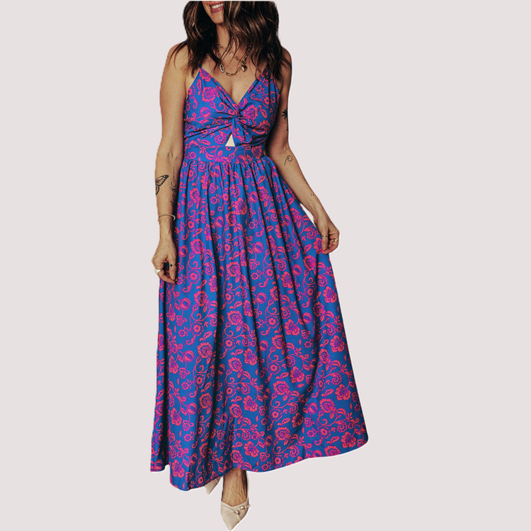Front view of a vibrant cobalt blue maxi dress featuring a pink floral print, twisted V-neckline, and waist cut-out on a clean neutral background.