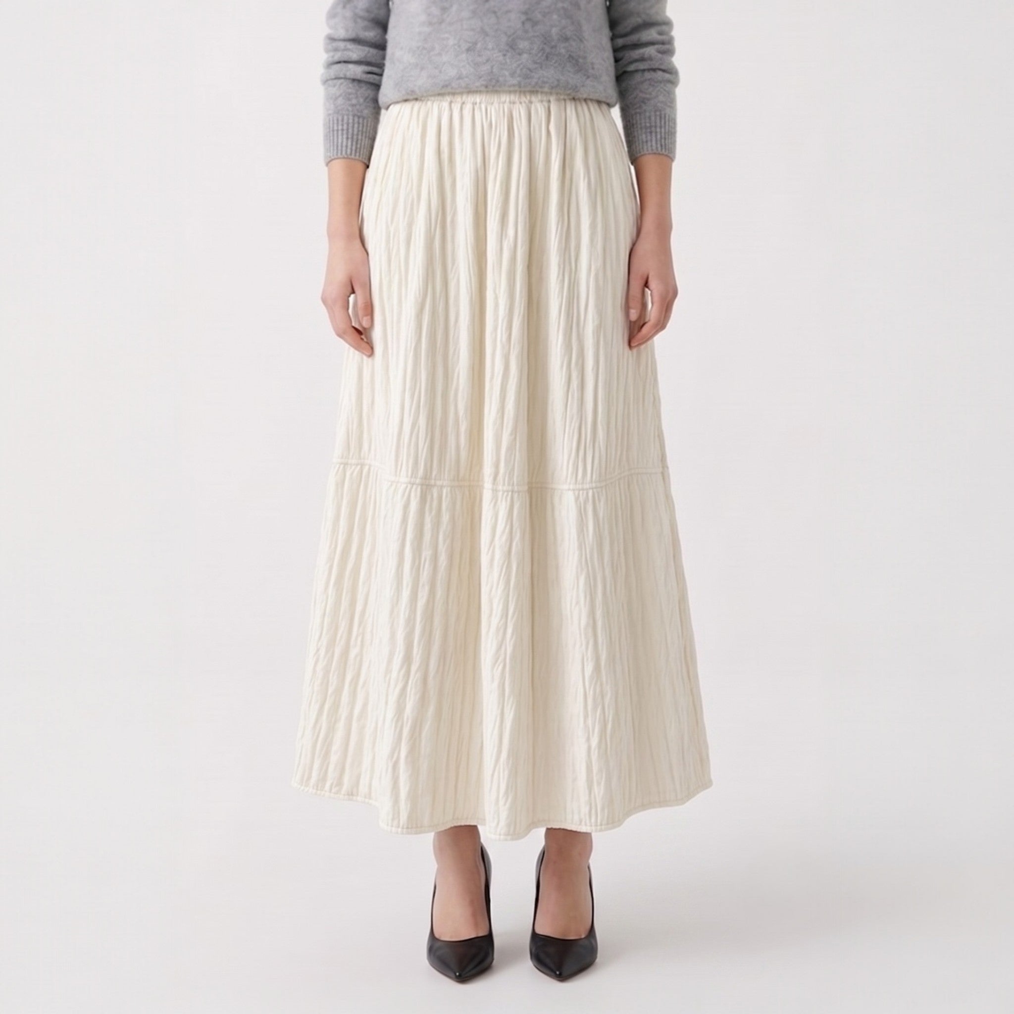 Person wearing a long ivory pleated skirt on a white background