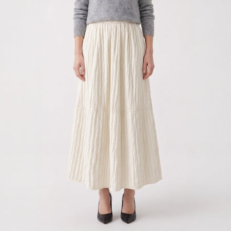 Person wearing a long ivory pleated skirt on a white background