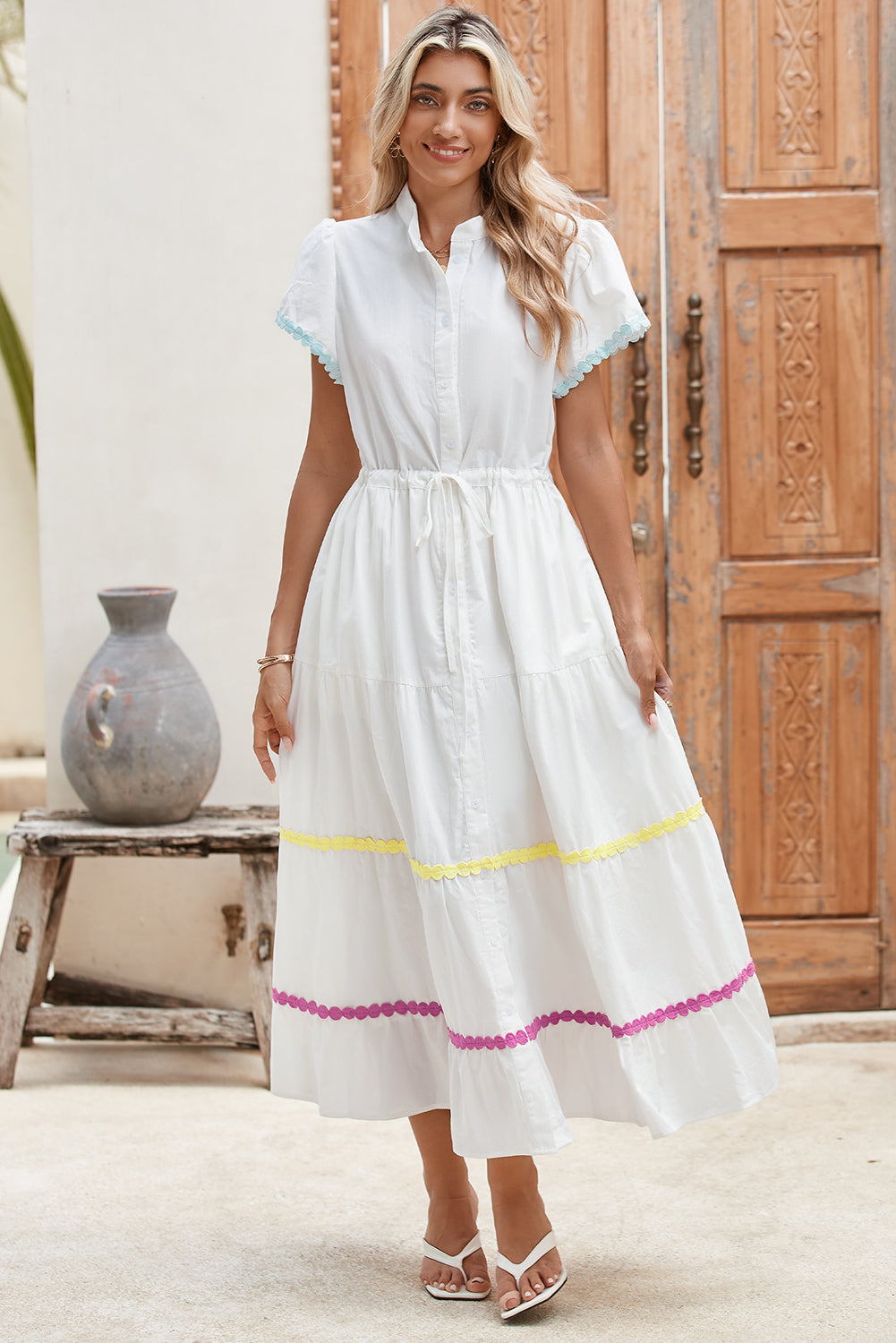 Model standing and smiling in a white tiered shirt dress with short sleeves and a waist tie, showcasing a stylish and cheerful look.