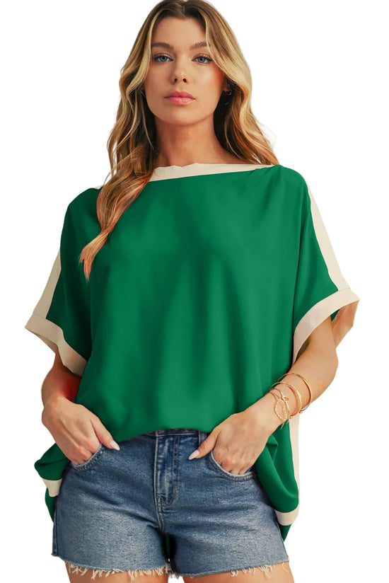 Woman wearing a green top with white trim and denim shorts against a beige background