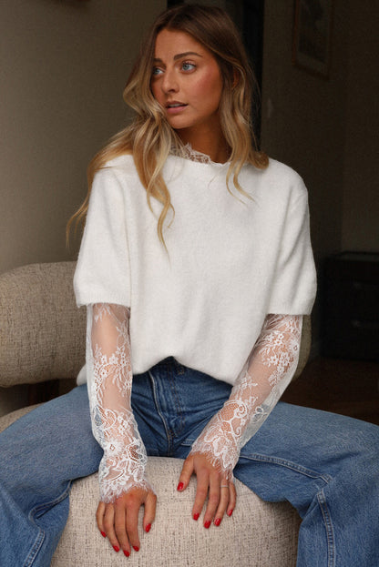 Woman wearing a white sweater with lace sleeves and blue jeans sitting on a couch.