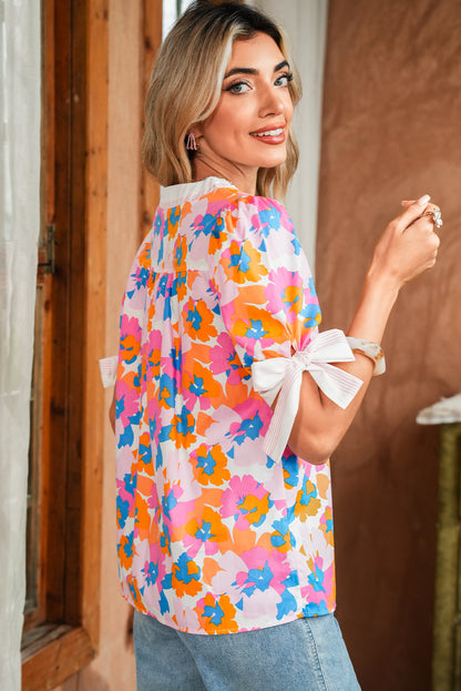 Woman wearing a colorful floral blouse with white bows, standing indoors.