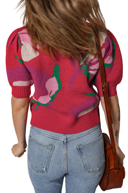 Person wearing a red floral sweater and blue jeans, holding a brown leather bag.
