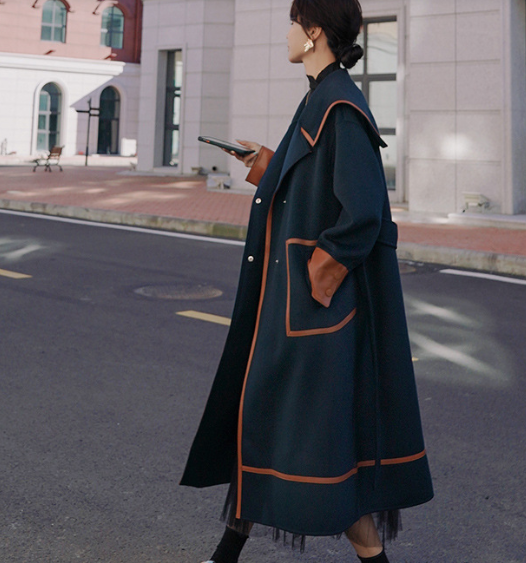 Person wearing a long dark coat with orange trim standing on a street.