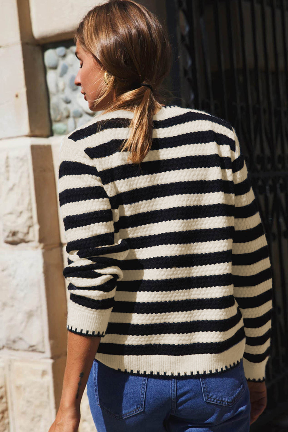 Person wearing a black and white striped sweater with a stone wall background