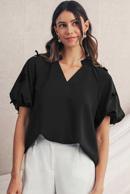 Woman wearing a black blouse with ruffled sleeves against a neutral background