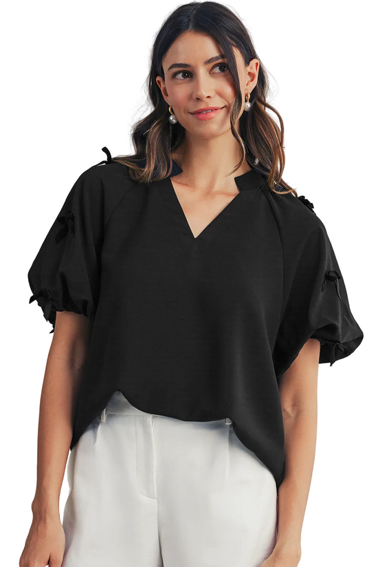 Woman wearing a black blouse with ruffled sleeves against a neutral background