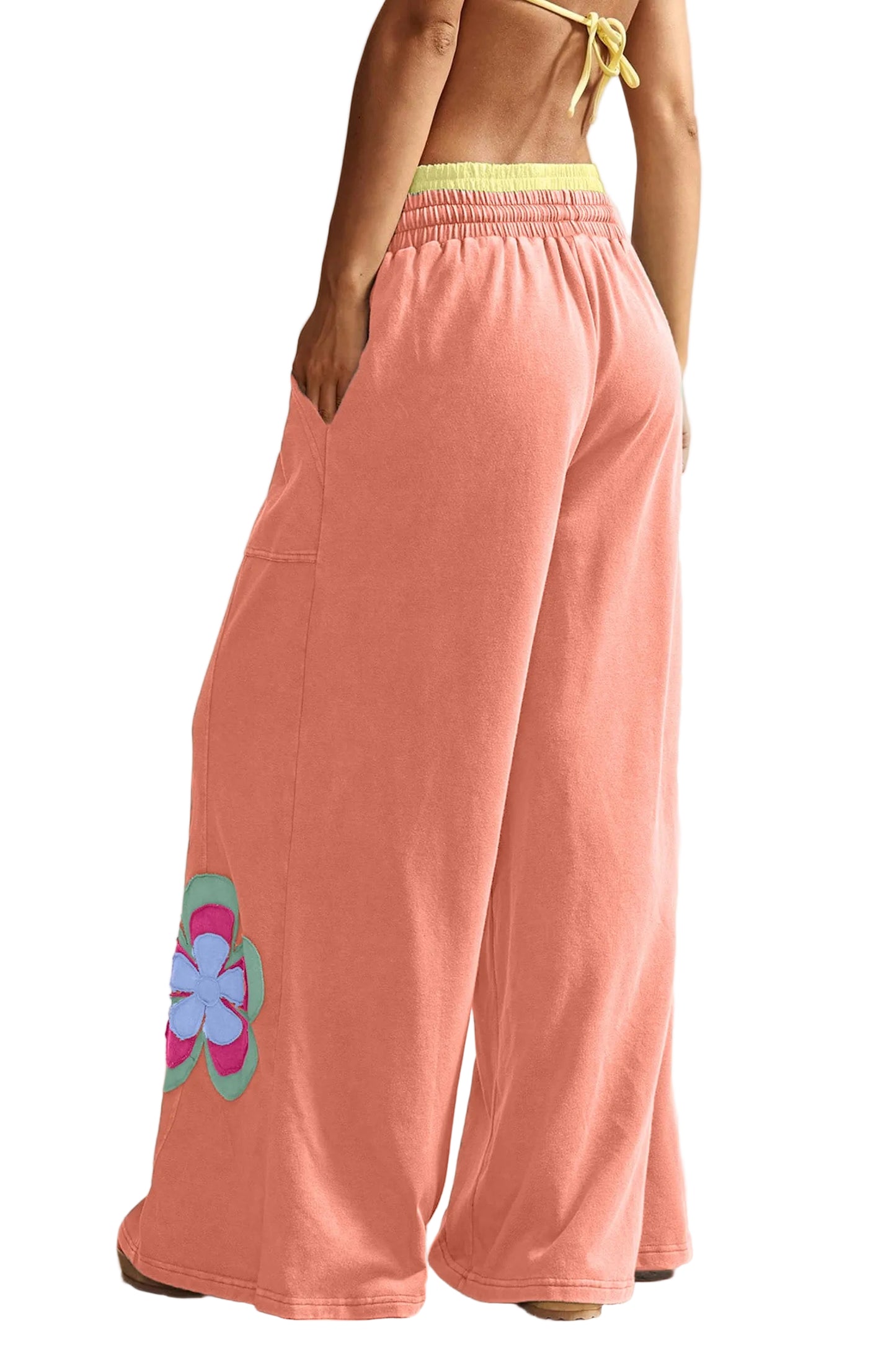 The rear view of the orange patchwork wide-leg pants on a model, highlighting the relaxed fit and the floral appliqué continuation near the hem.
