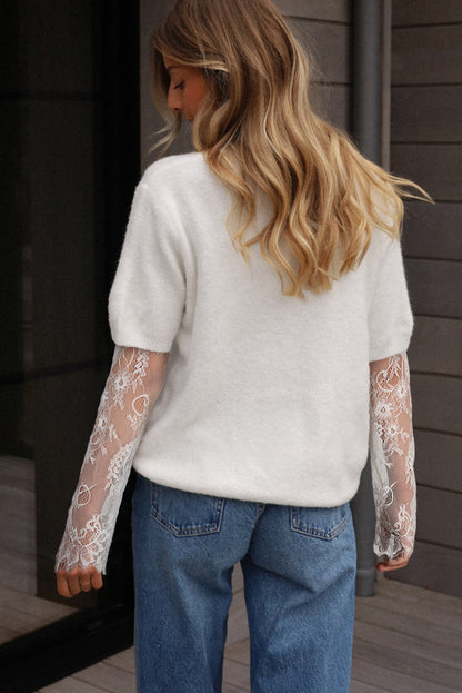Person wearing a white sweater with lace sleeves and blue jeans, standing against a wooden wall.
