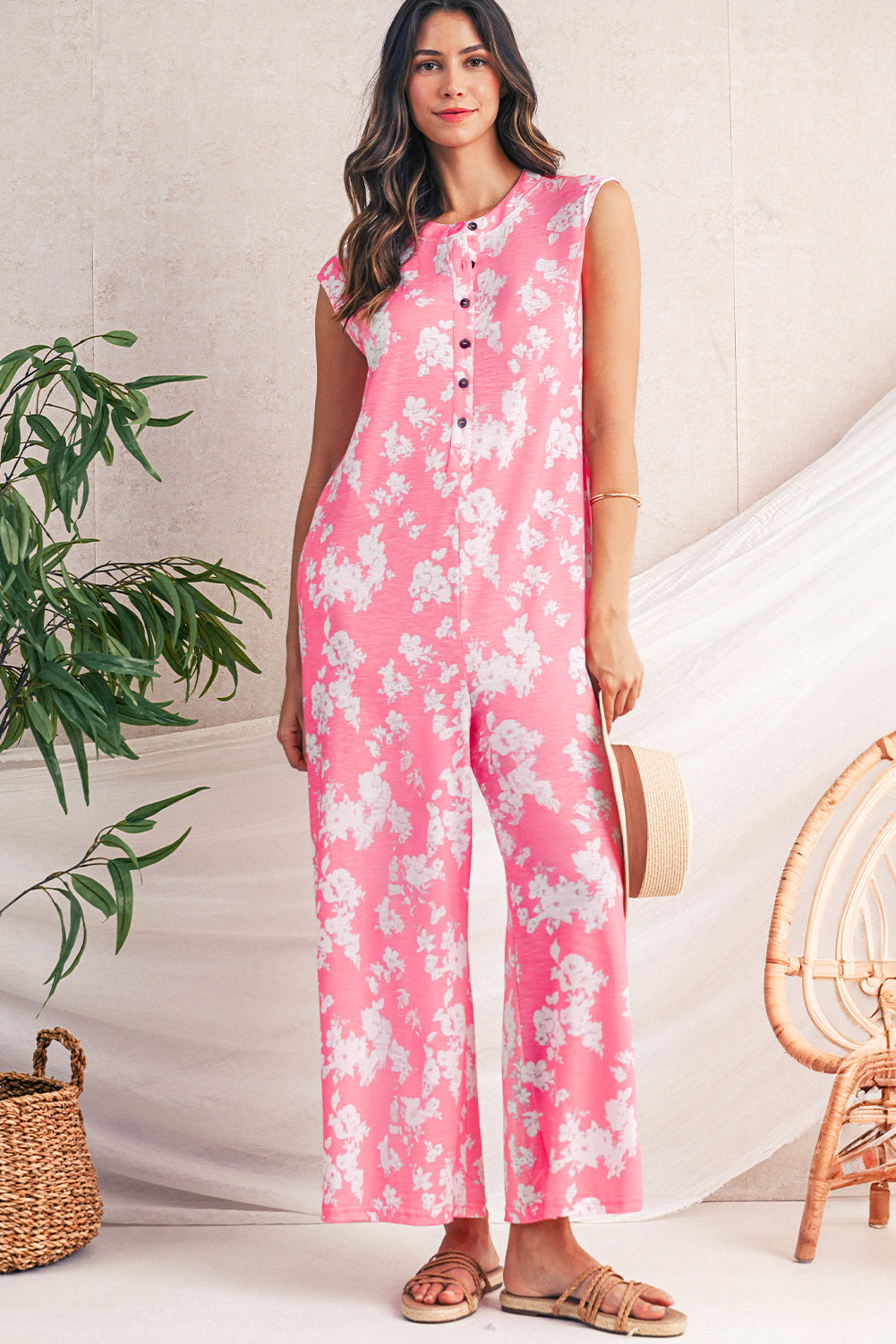 Woman wearing a pink floral jumpsuit standing in a room with a plant and chair.