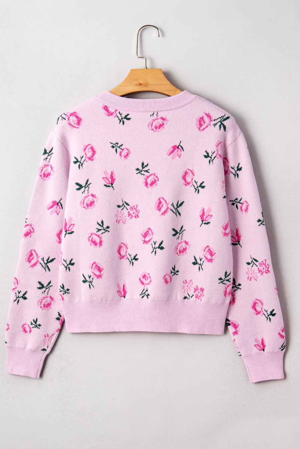 Pink sweatshirt with floral pattern on a hanger against a light gray background