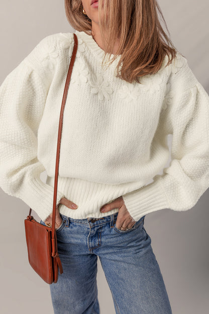 Person wearing a white sweater and blue jeans with a brown leather bag on a plain background