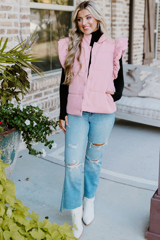 Woman wearing a pink vest, black turtleneck, and blue jeans on a patio.