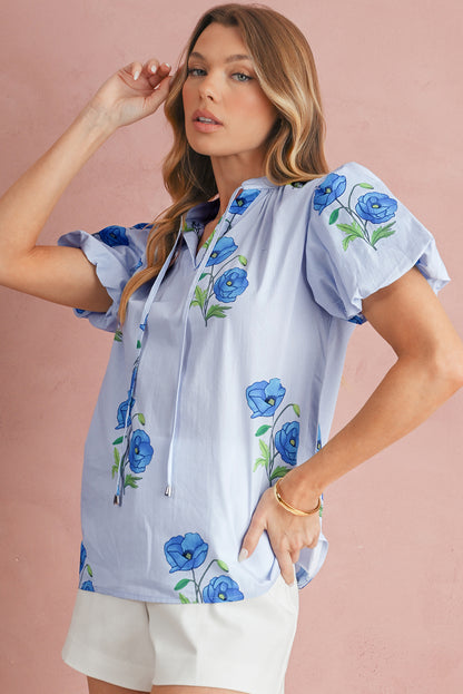 Woman wearing a light blue blouse with floral embroidery on a pink background