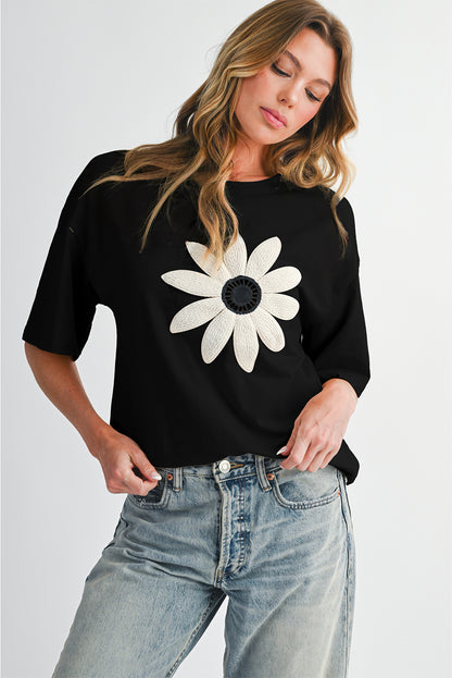 Woman wearing a black t-shirt with a white flower design on a plain background