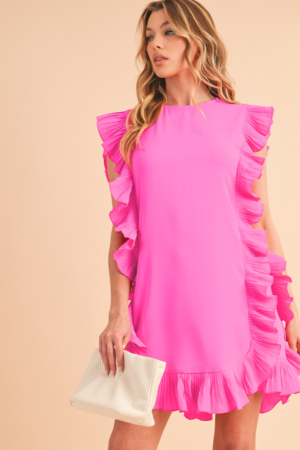 Front view of bright pink short-sleeve dress with elegant ruffle details on a model holding a cream fabric clutch, looking to her right, perfect for spring and summer special occasions.