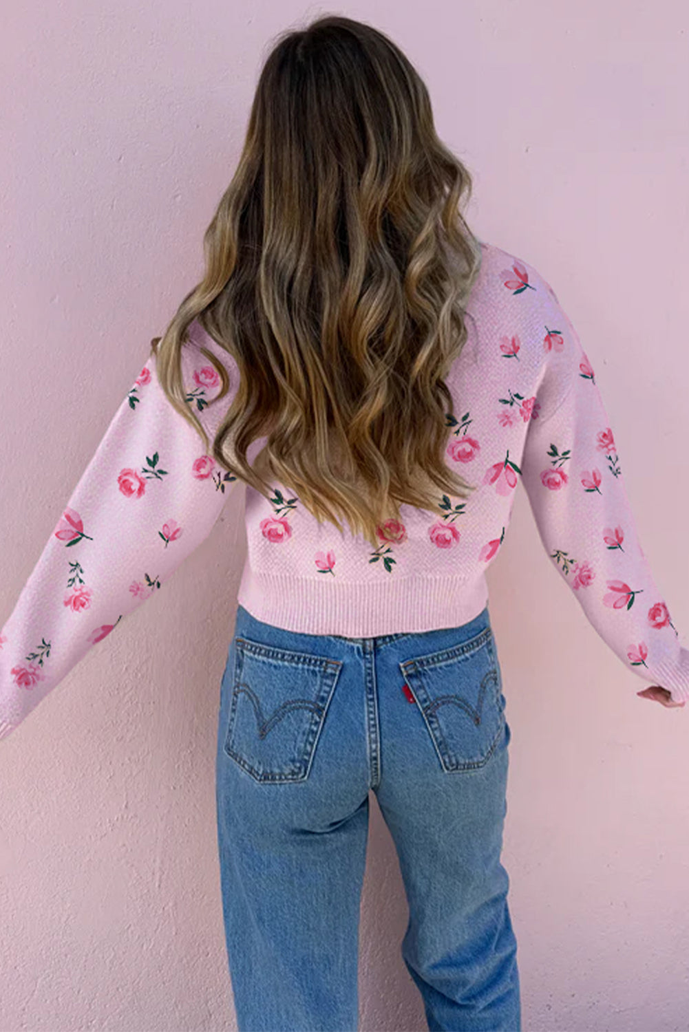 Person wearing a pink floral sweater and blue jeans against a light pink background