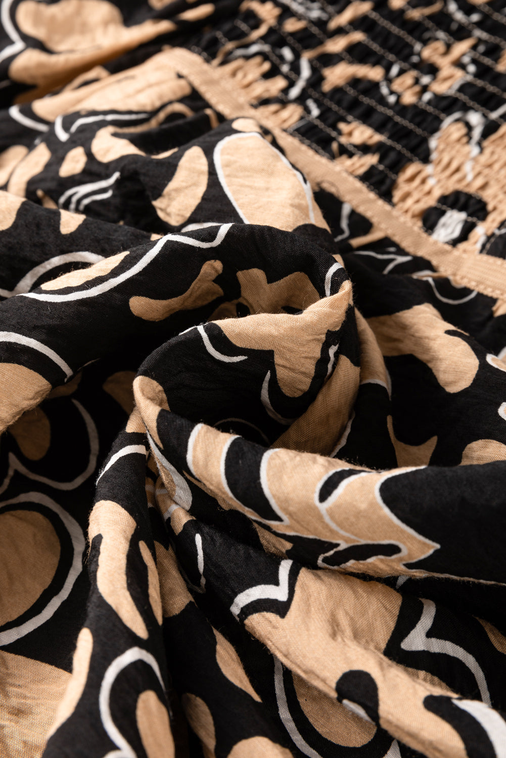 Close-up fabric view of a black floral boho blouse with a front lace-up split neckline and half sleeves.