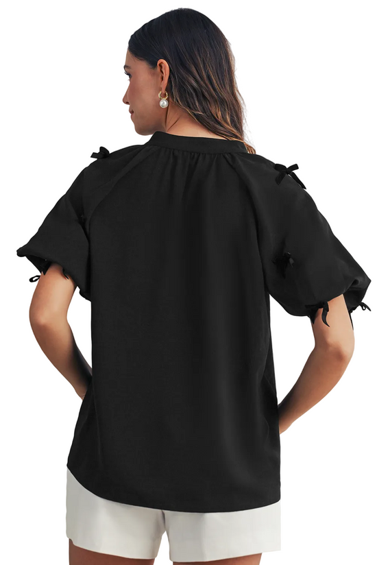 Woman wearing a black blouse with bow details on a neutral background