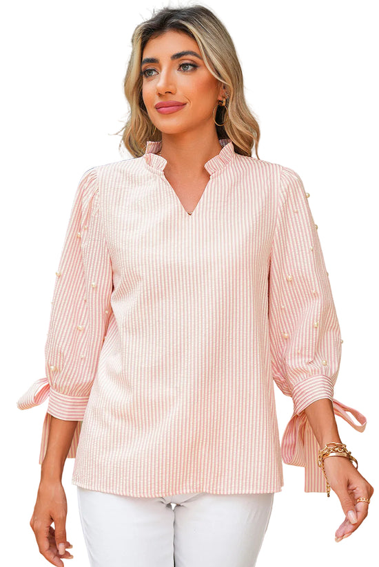Woman wearing a light pink striped blouse with tied sleeves outdoors.