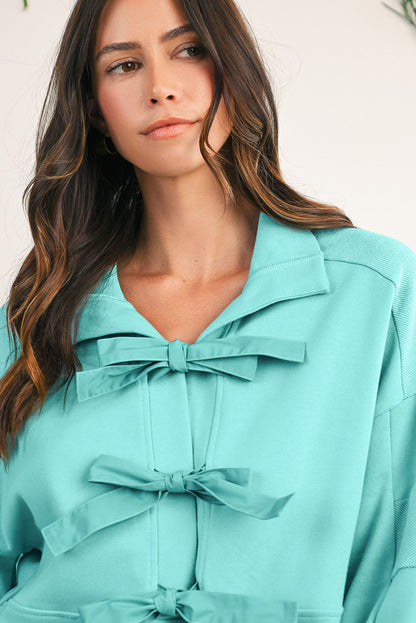 Woman wearing a turquoise dress with bow details against a neutral background