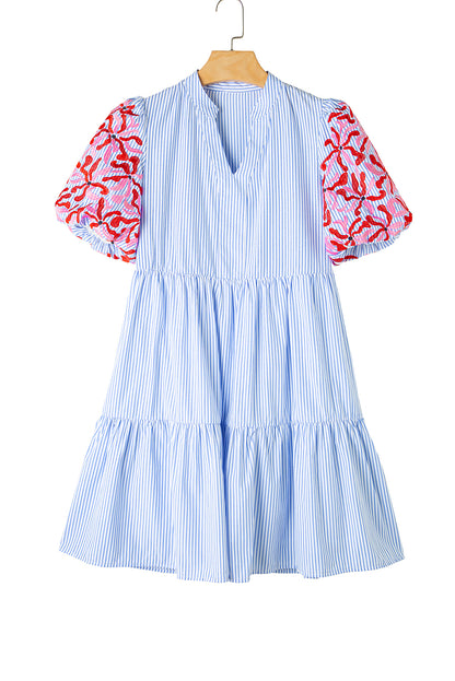 Front view of blue striped tiered mini dress with floral red and pink puff sleeves on white background.