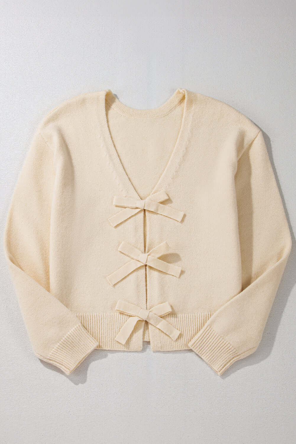 Flat lay of a cream knit cardigan with bow details, ideal for casual or dressy outfits.
