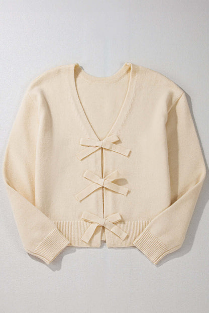 Flat lay of a cream knit cardigan with bow details, ideal for casual or dressy outfits.
