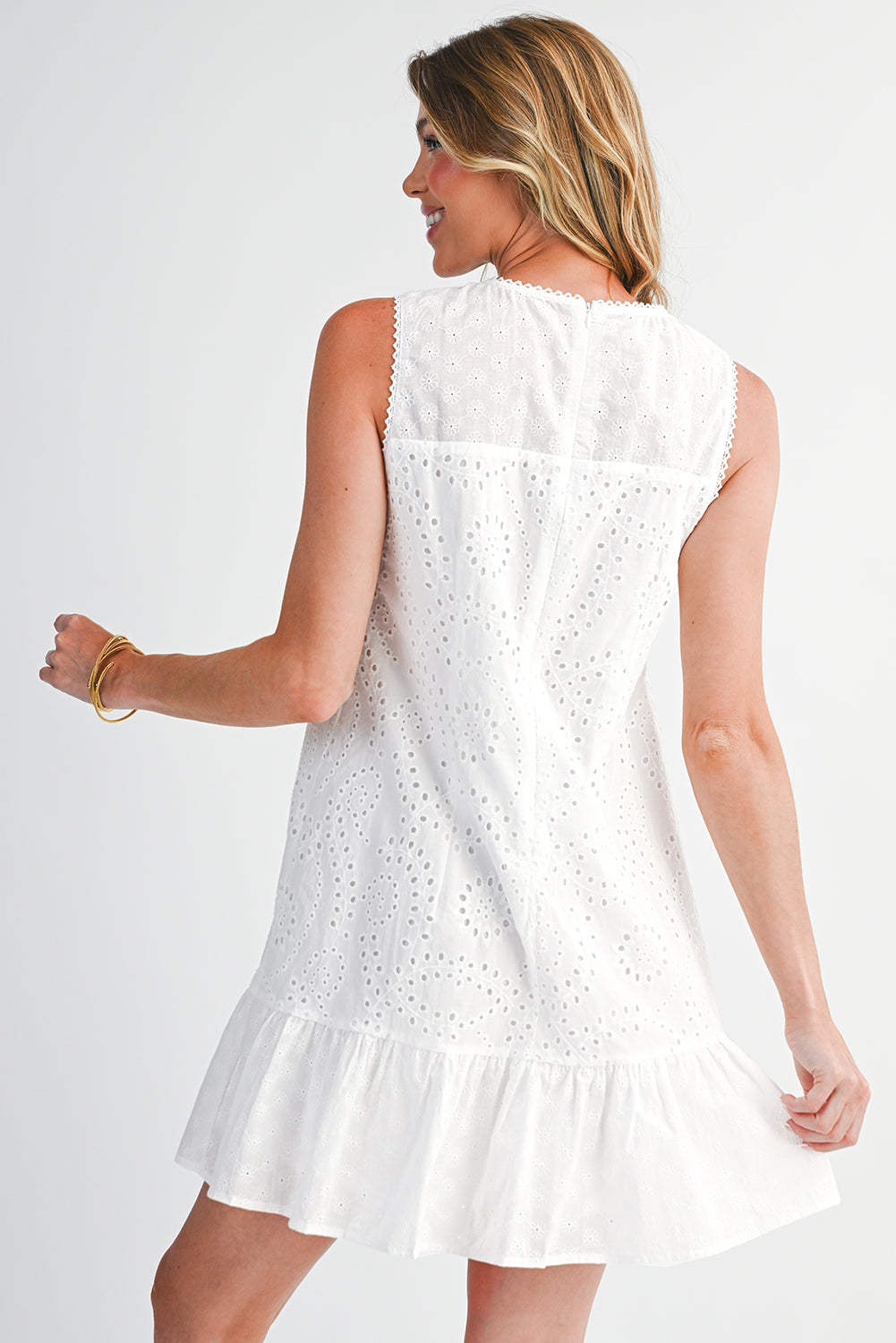 Woman wearing a white dress with eyelet details on a plain background